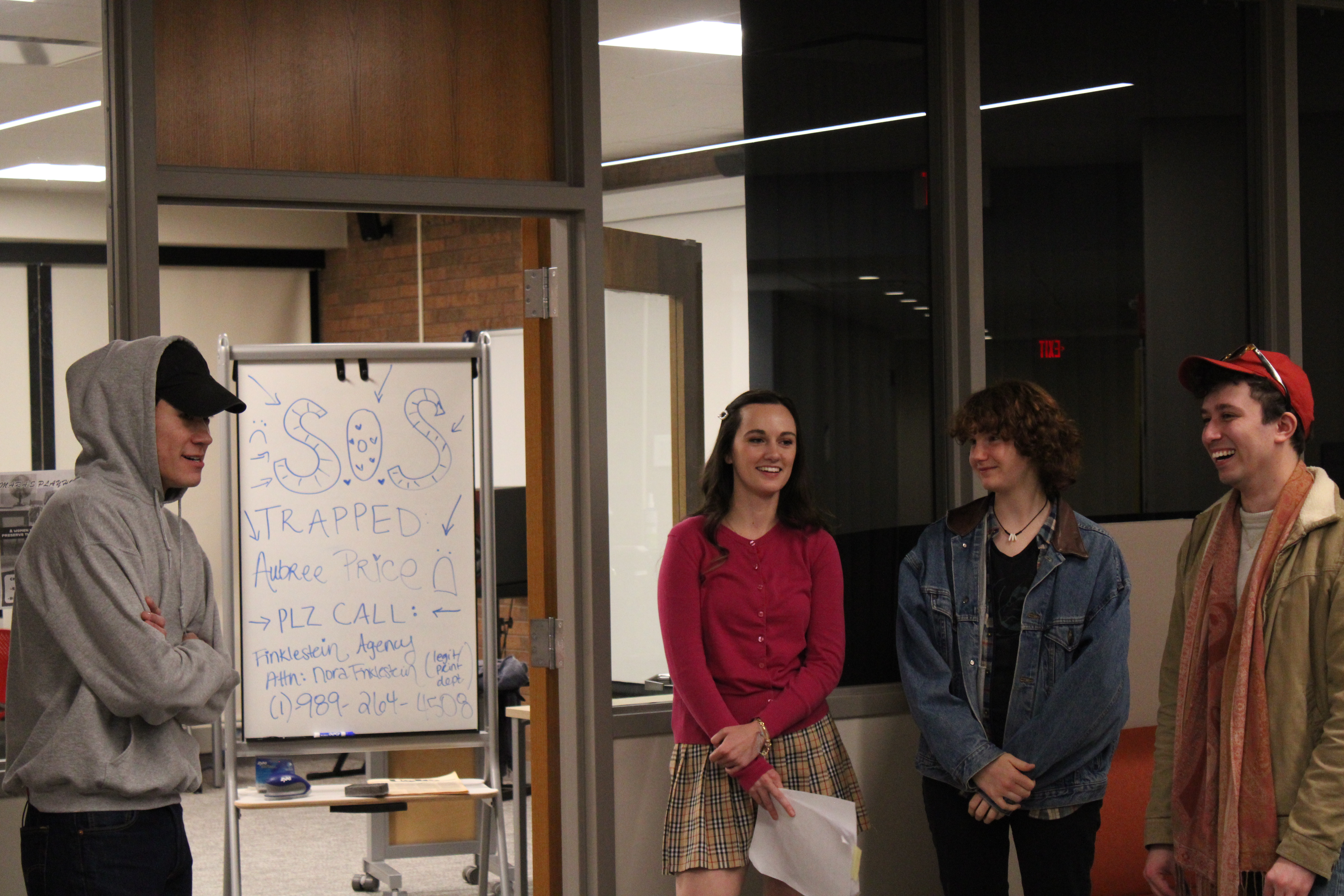 The cast gathers around a white board from the film that reads S.O.S.